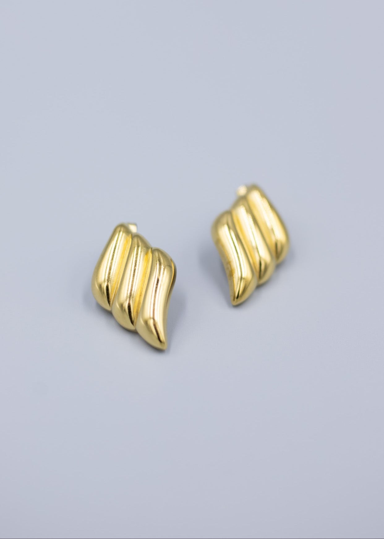 triple wave 18k gold stud earrings laid flat on a light gray background