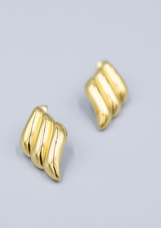 Close up of a pair of 18k gold triple wave stud earrings on a light gray background