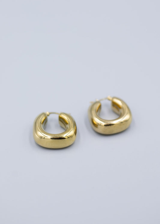 Angled view of 18k gold plated horseshoe hoof hoop earrings laid flat on a light gray background