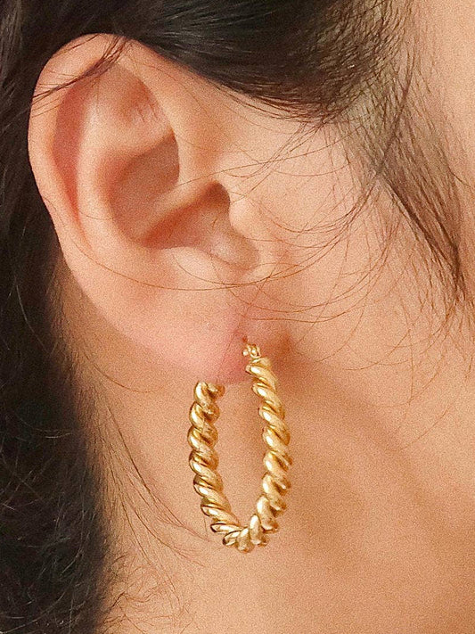 Close-up of a person wearing gold hoop earrings with a neutral background