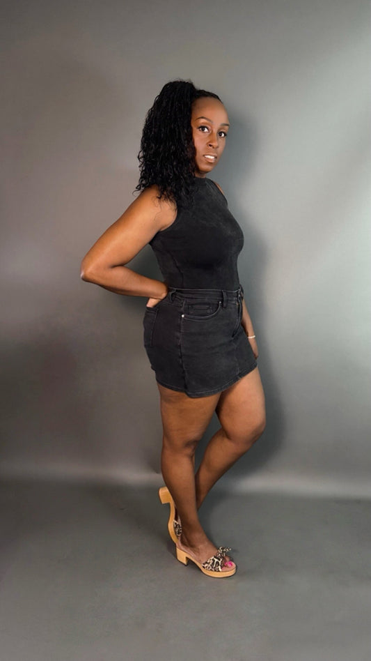 Side view of a woman wearing a black mock neck bodysuit top and faded black skorts against a dark gray background.
