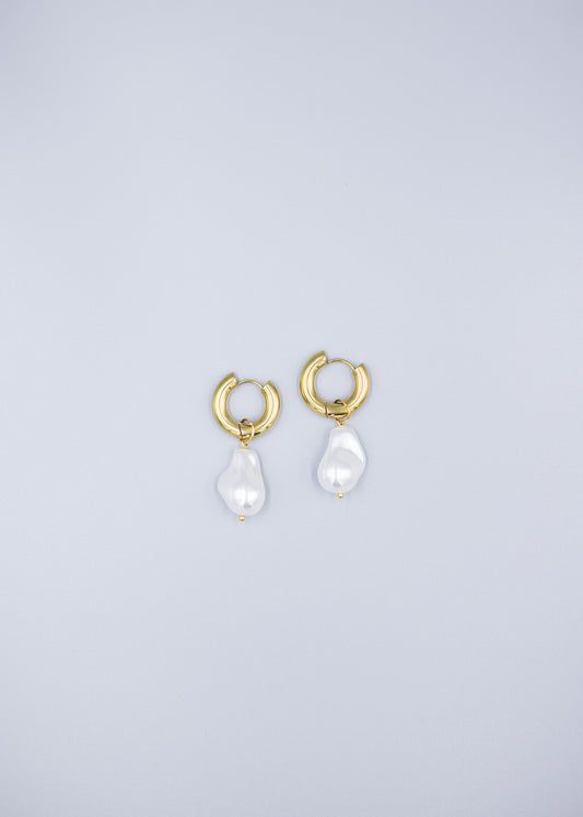 Distant view of a pair of 18k gold plated hoop earrings with removable dropped baroque pearls laid flat on a light gray background