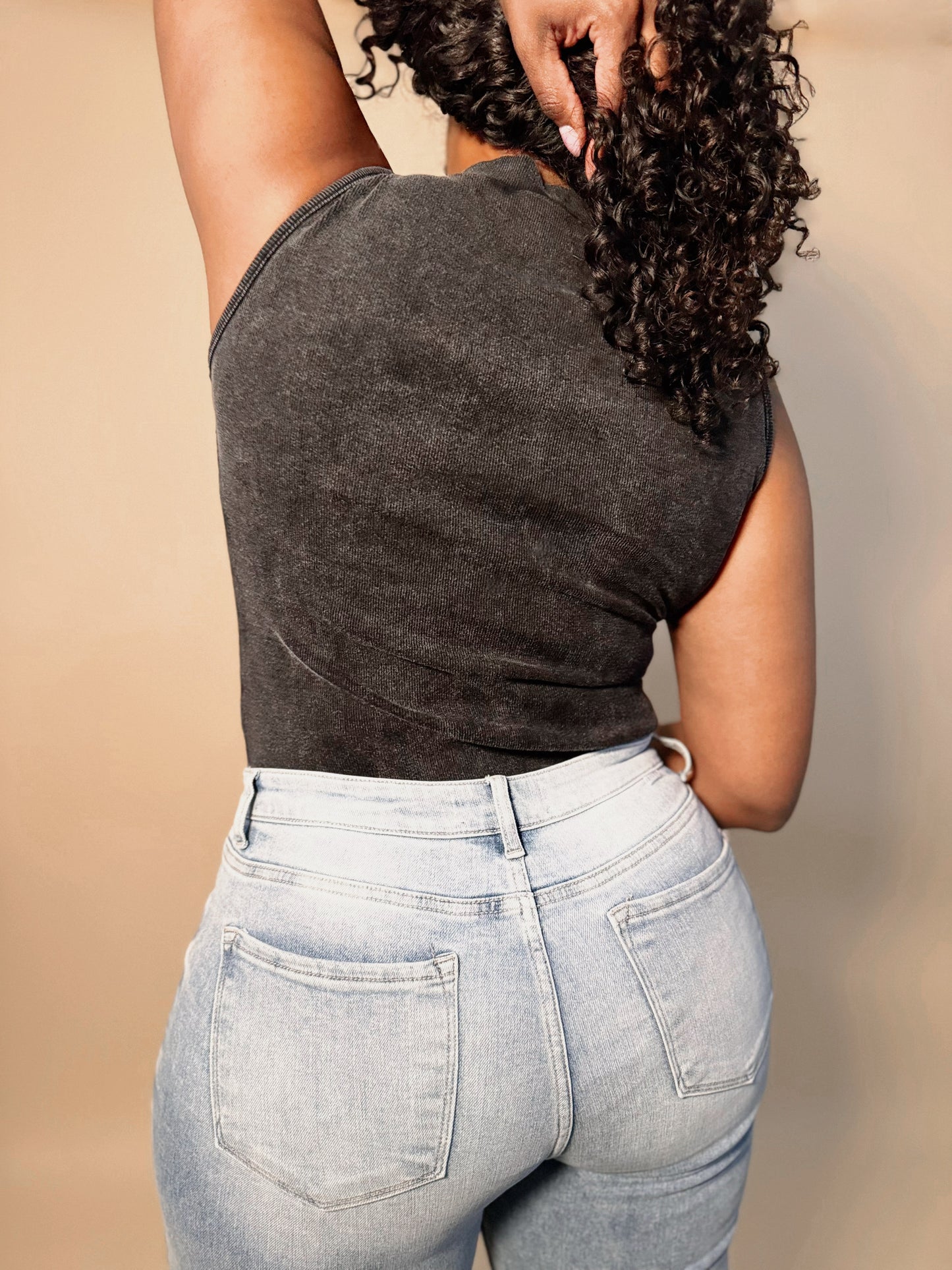 Back view of a women's elevated casual top black mineral washed mock neck bodysuit top, showcasing its relaxed silhouette, subtle distressing, and modern minimalist design for effortless style.