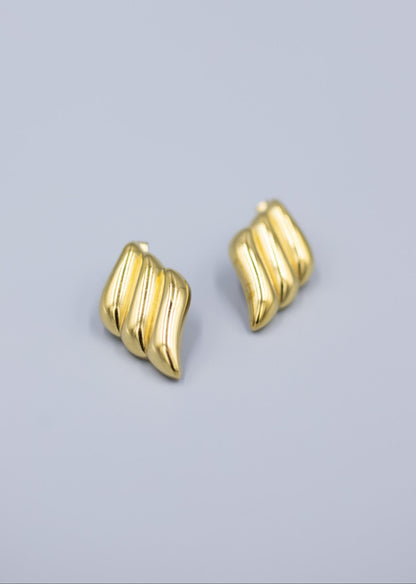triple wave 18k gold stud earrings laid flat on a light gray background