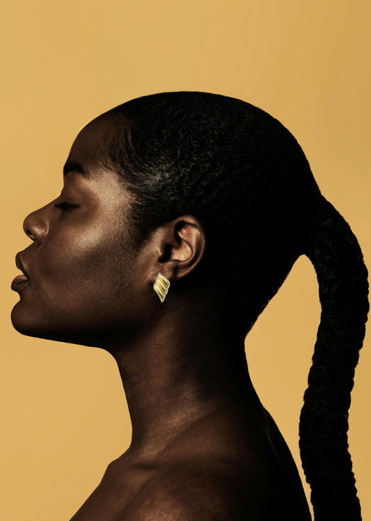 Side profile of a black woman with 18k gold triple wave 18k gold stud earrings against a beige background