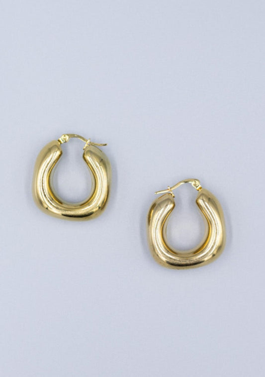 Close up of 18k gold plated horseshoe hoof hoop earrings on a light gray background