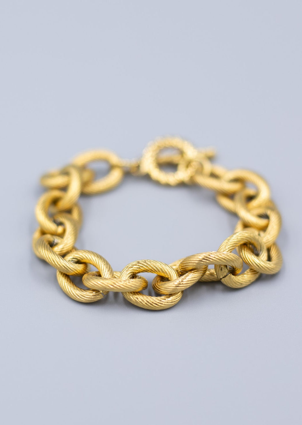 Close up of a textured 18k gold plated link chain bracelet on a light gray background