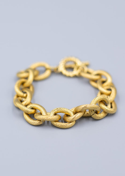Close up of a textured 18k gold plated link chain bracelet on a light gray background