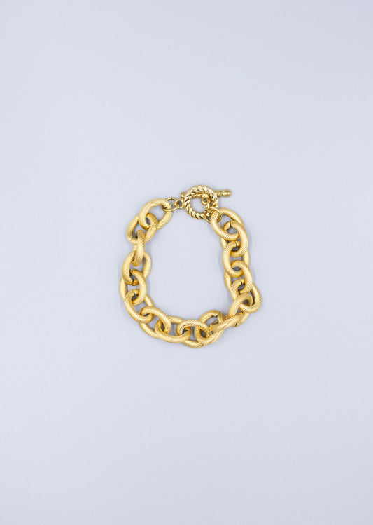 Birds-eye view of a 18k gold plated textured link chain bracelet laid flag on a light gray background