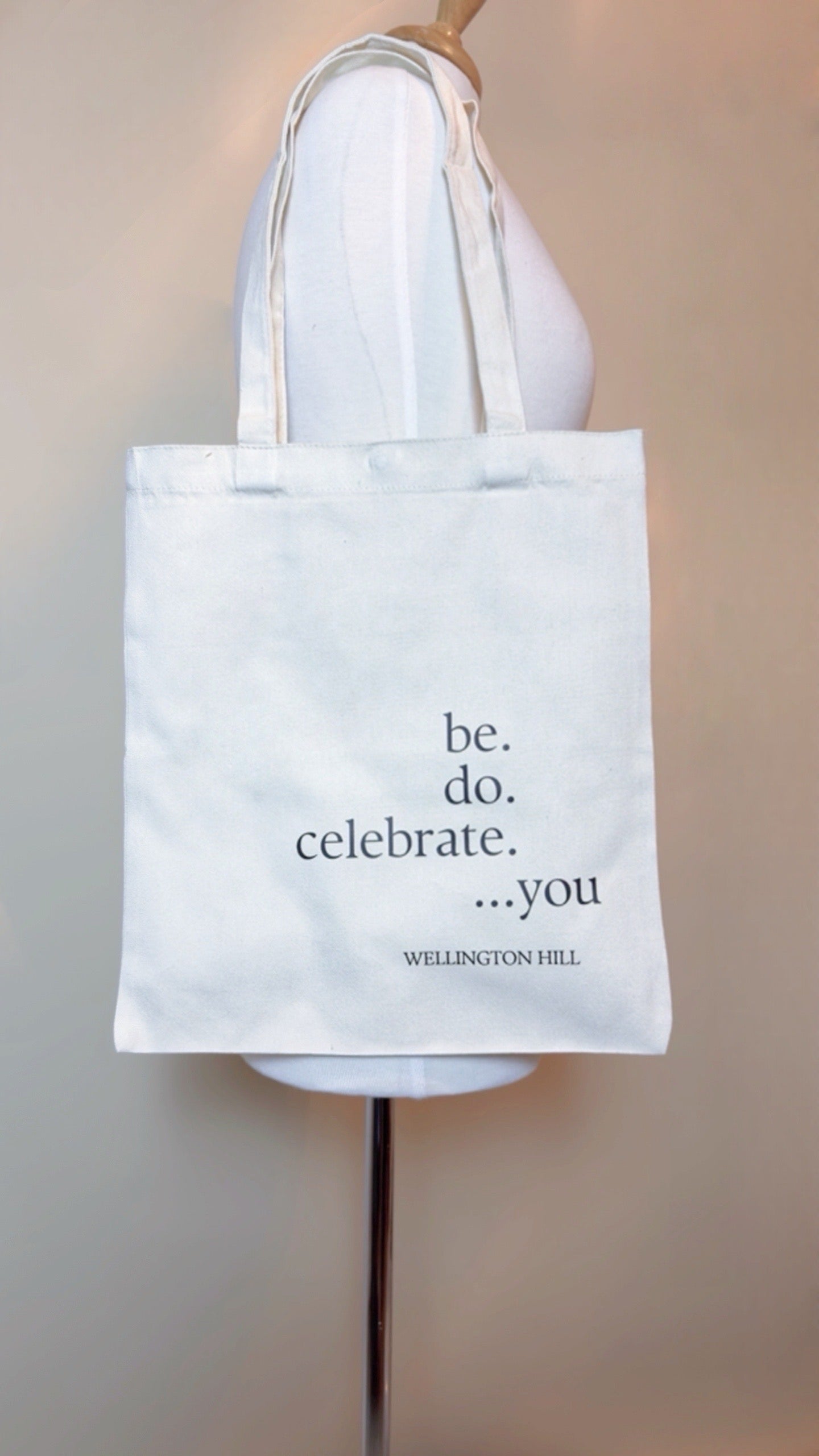 Tote bag with motivational quote 'be. do. celebrate. ...you' held by a person.