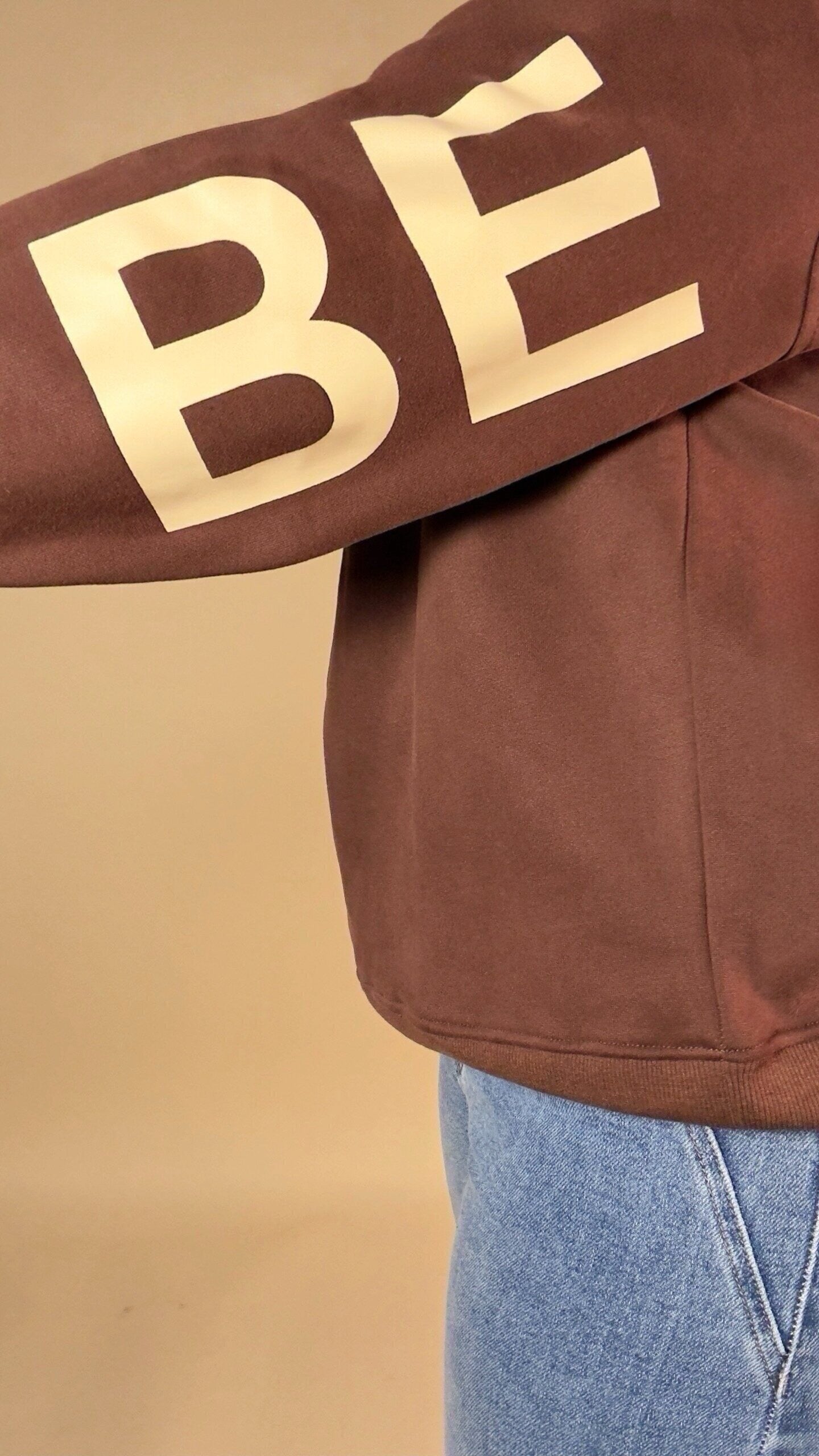 BE YOURSELF sleeve sweatshirt featuring a brown sleeve with 'Bé' lettering on a beige background