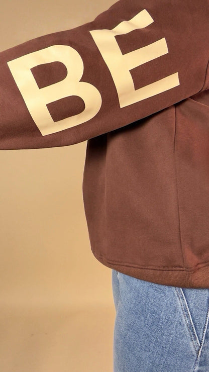 BE YOURSELF sleeve sweatshirt featuring a brown sleeve with 'Bé' lettering on a beige background