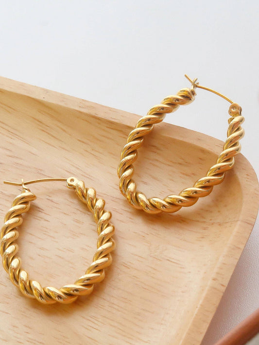 Gold hoop earrings on a wooden tray with a white background