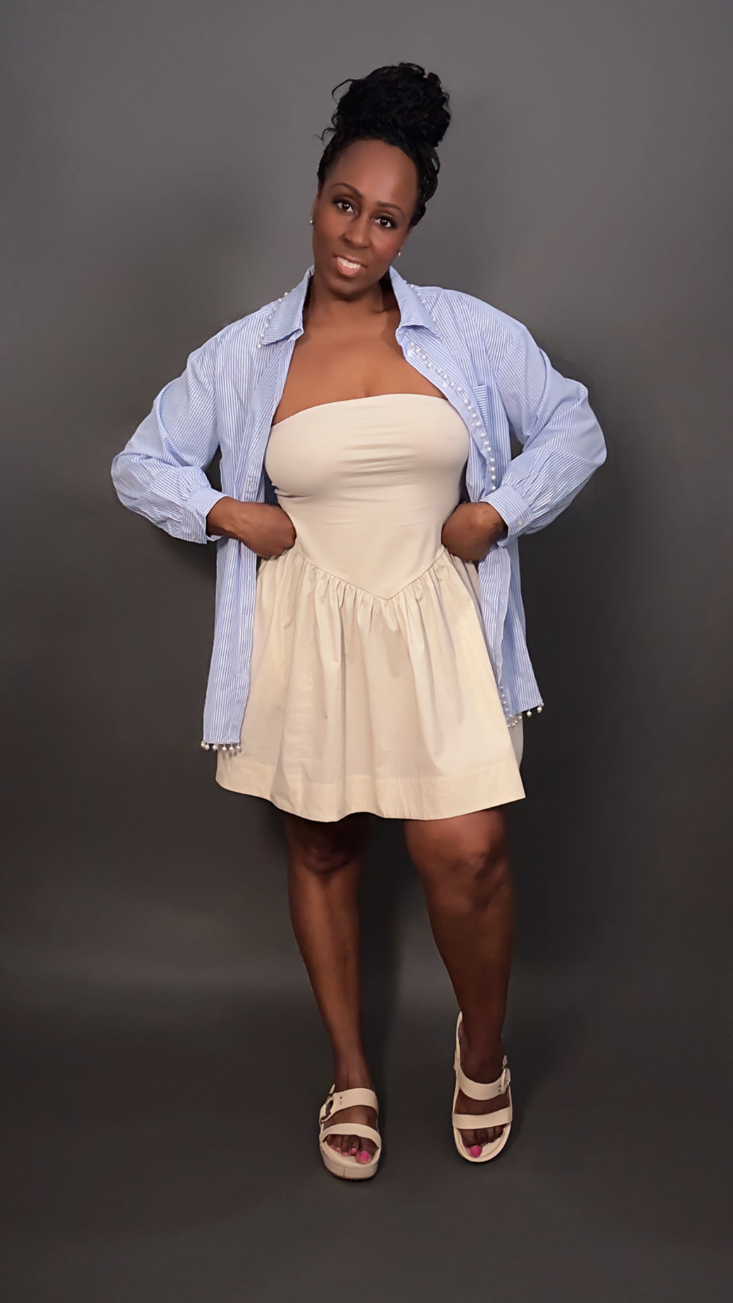 Woman wearing a faux pearl trimmed blue and white stripped oversized button-down shirt unbuttoned and layered over a cream dress, spring outfit style for women
