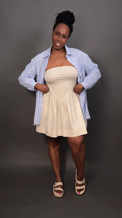 Woman wearing a faux pearl trimmed blue and white stripped oversized button-down shirt unbuttoned and layered over a cream dress, spring outfit style for women