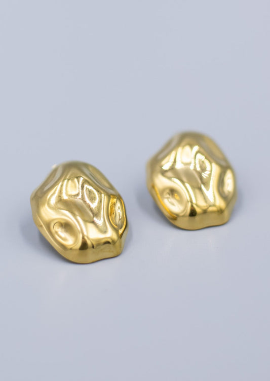 a close up of a pair of 18k gold plated hammered stud earrings laid flat on a light gray background