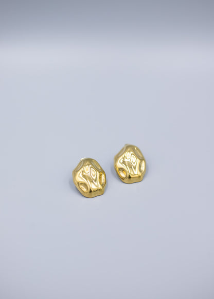 Angled view of a pair of 18k gold plated hammered stud earrings on a light gray background