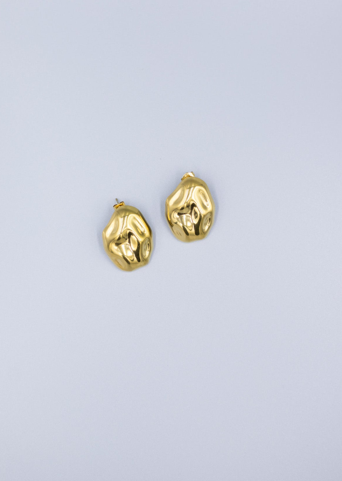 zoomed out pair of 18k gold plated hammered stud earrings laid flat on a light gray background 