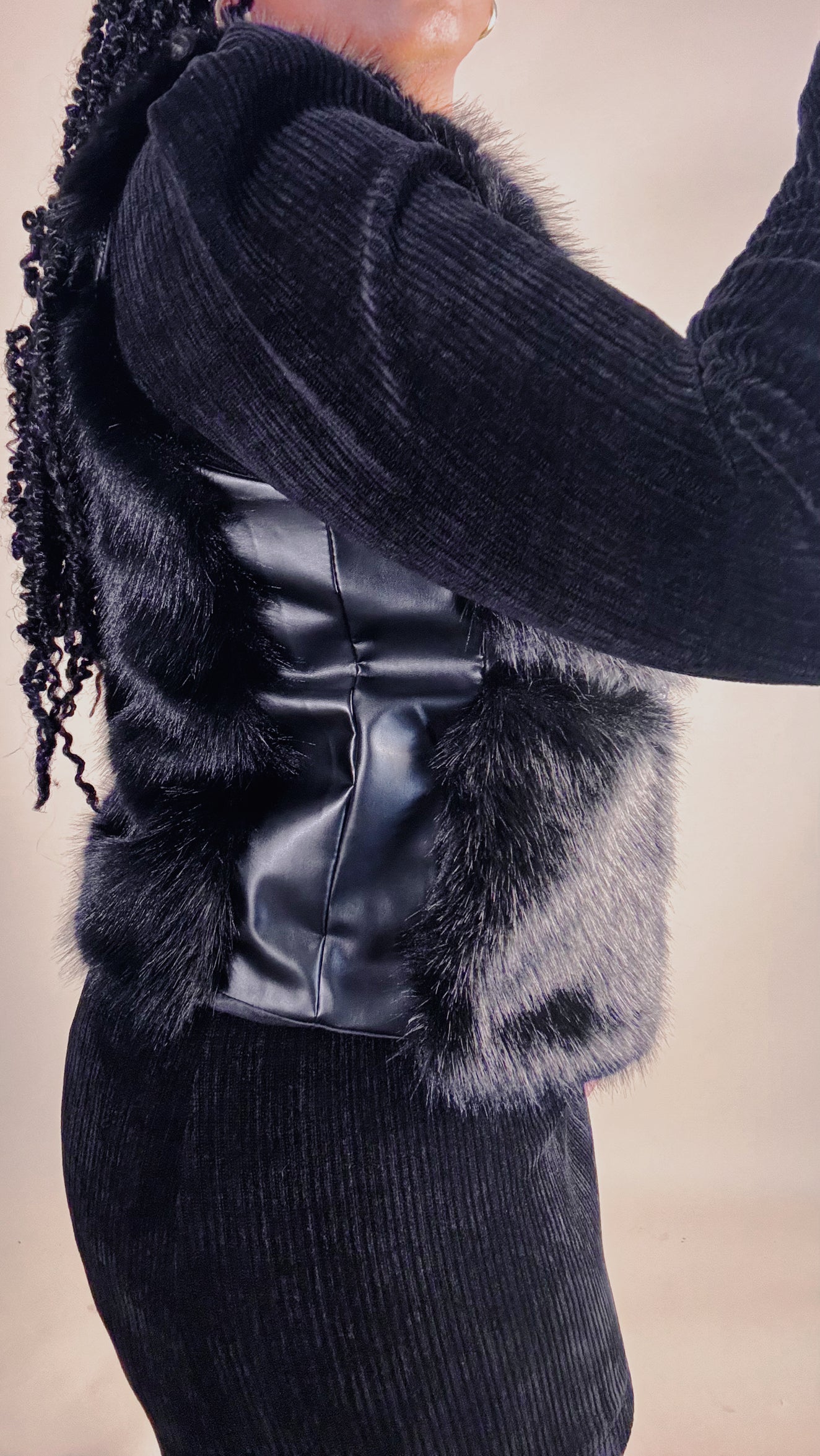 Black fur vest with faux leather trim worn by a black woman on a neutral background