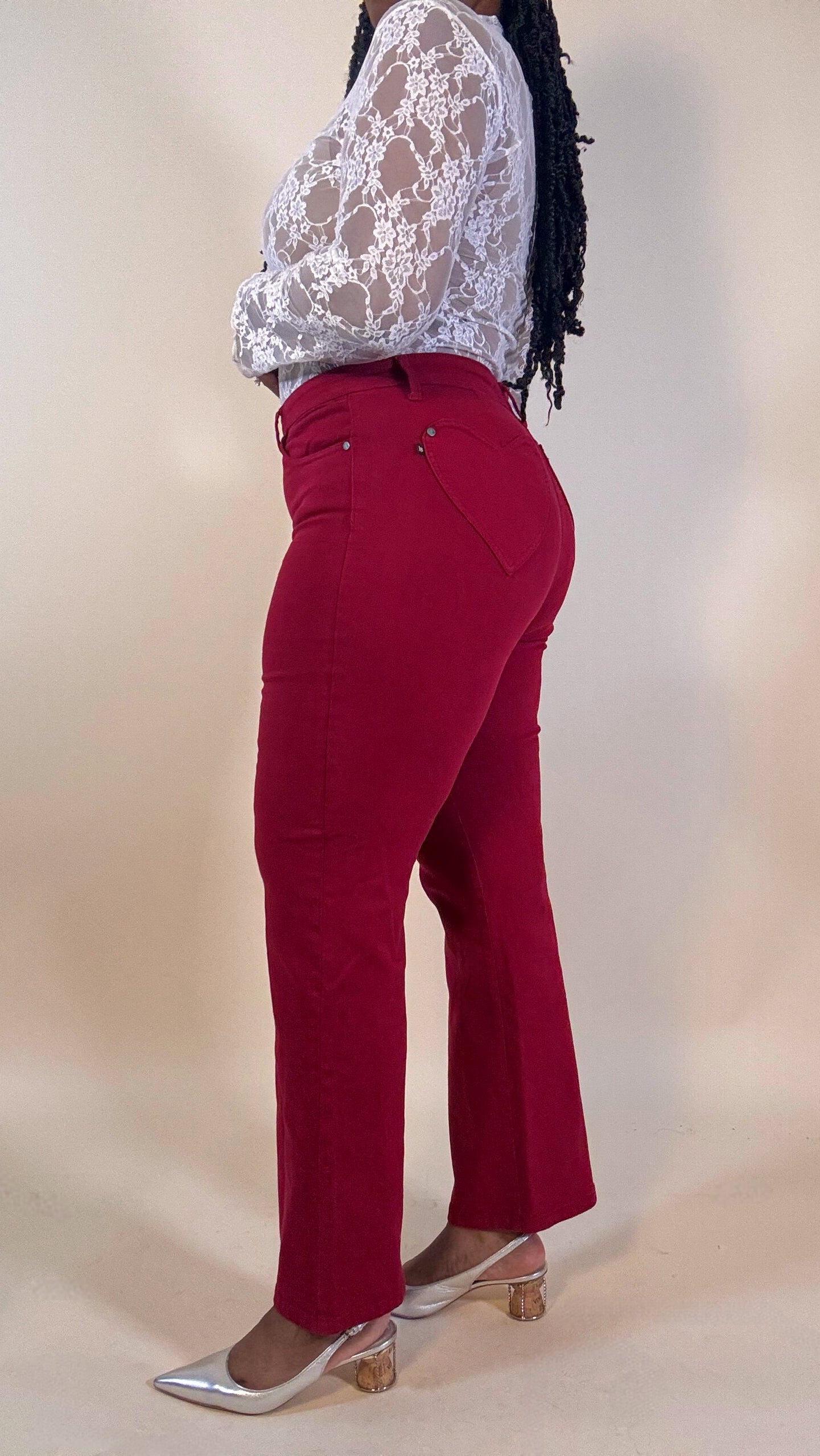 Woman wearing red heart shaped pocket jeans and a white lace top on a beige background