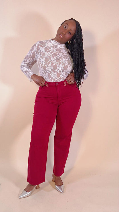 Woman wearing a white lace top and red jeans on a beige background