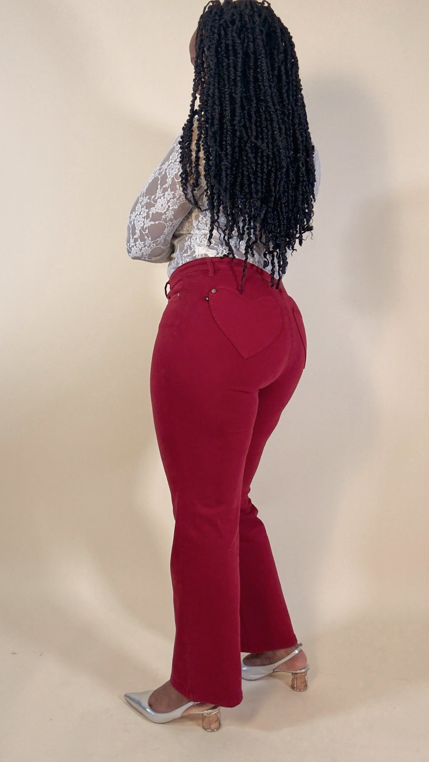 Woman wearing red jeans with heart and a white lace top on a beige background
