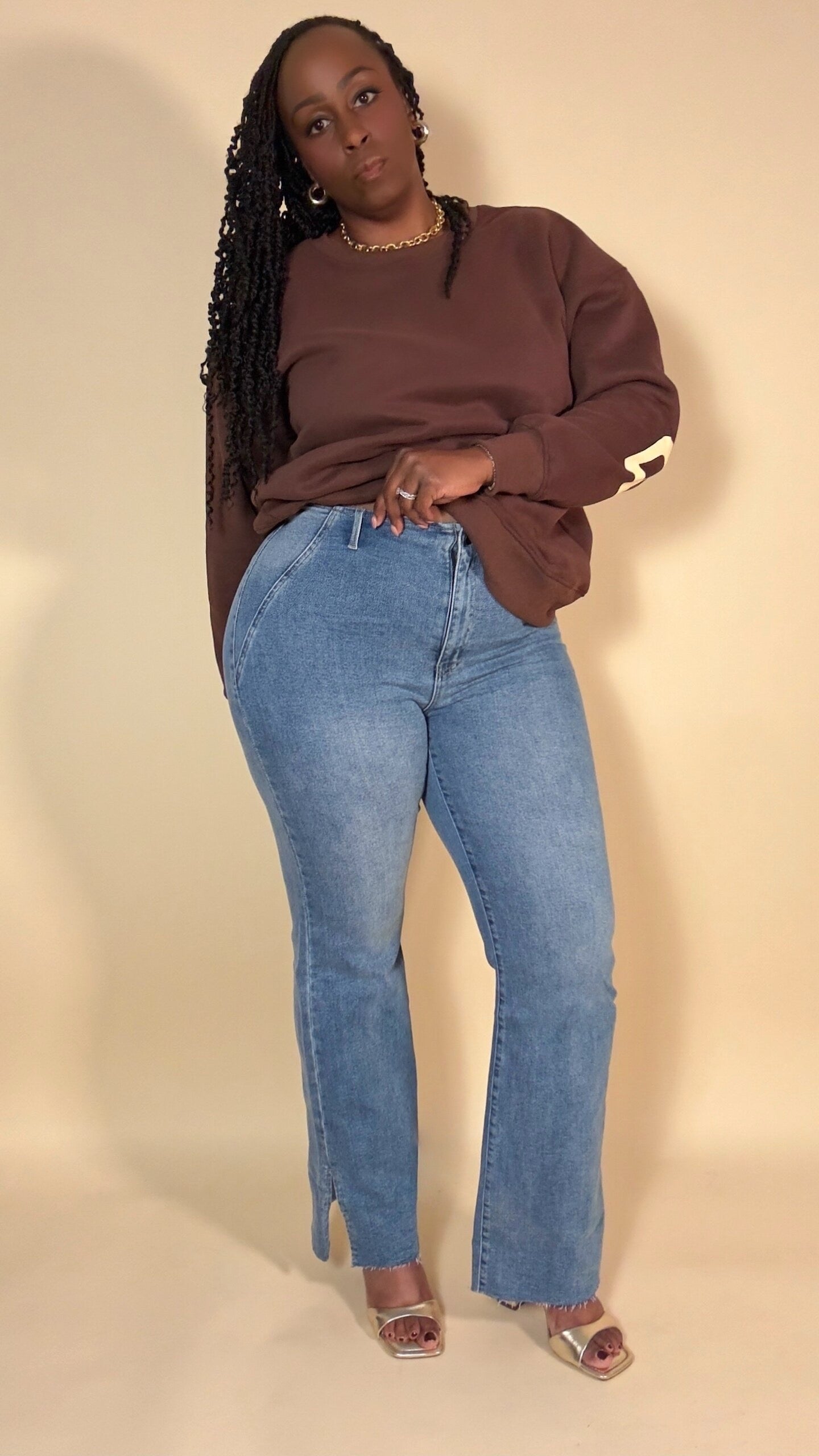 Person wearing a brown sweatshirt with "be yourself love yourself" text in beige and blue jeans with a slit against a beige background