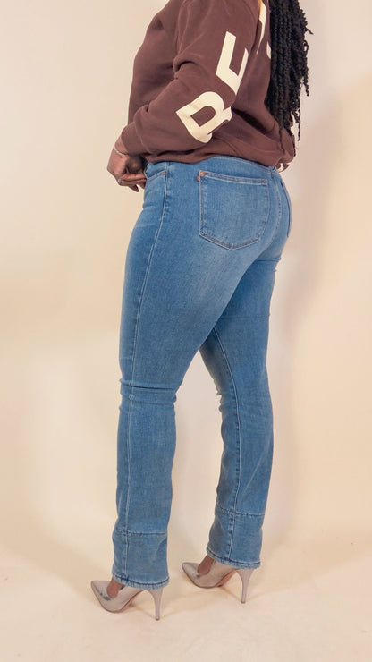 Person wearing blue jeans and a brown sweatshirt with letters against a beige background