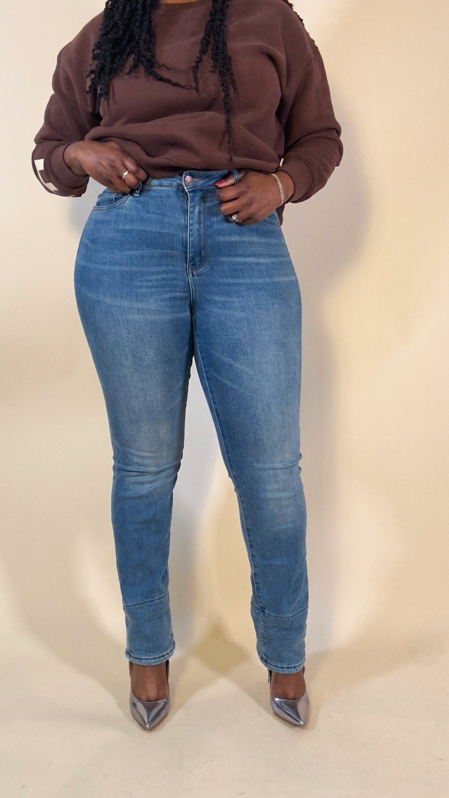 Person wearing a brown sweatshirt and blue jeans on a beige background