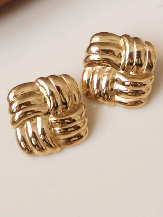 Gold knitted earrings on a light surface background