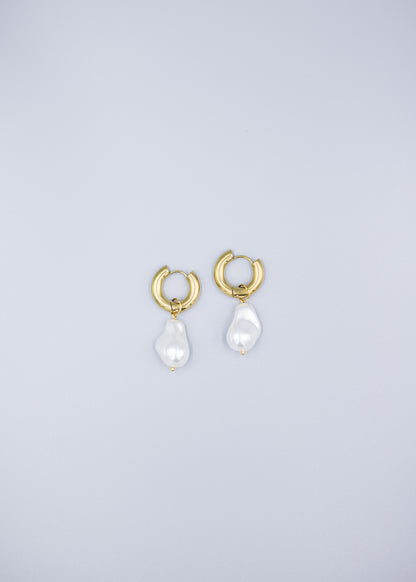 Distant view of a pair of 18k gold plated hoop earrings with removable dropped baroque pearls laid flat on a light gray background