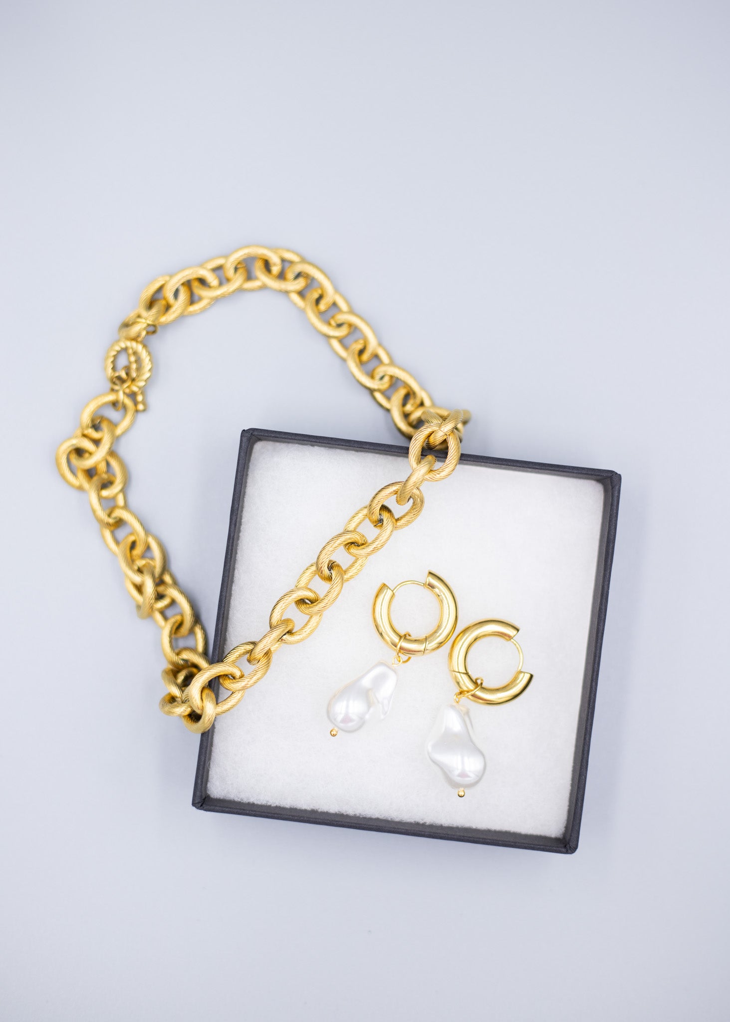 An 18k gold necklace paired with 18k gold plated hoop earrings with dropped pearls in a jewelry box with a white background