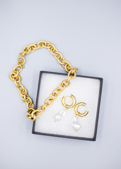 An 18k gold necklace paired with 18k gold plated hoop earrings with dropped pearls in a jewelry box with a white background