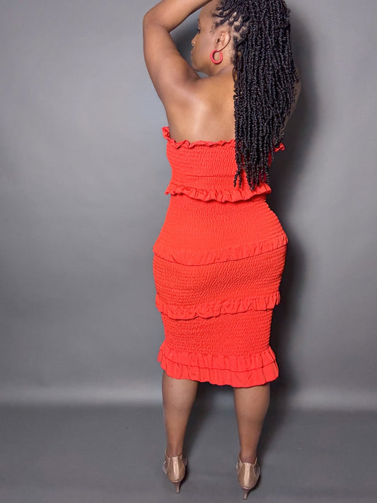 Woman wearing a red smocked shirred midi tube dress with ruffled details against a gray background