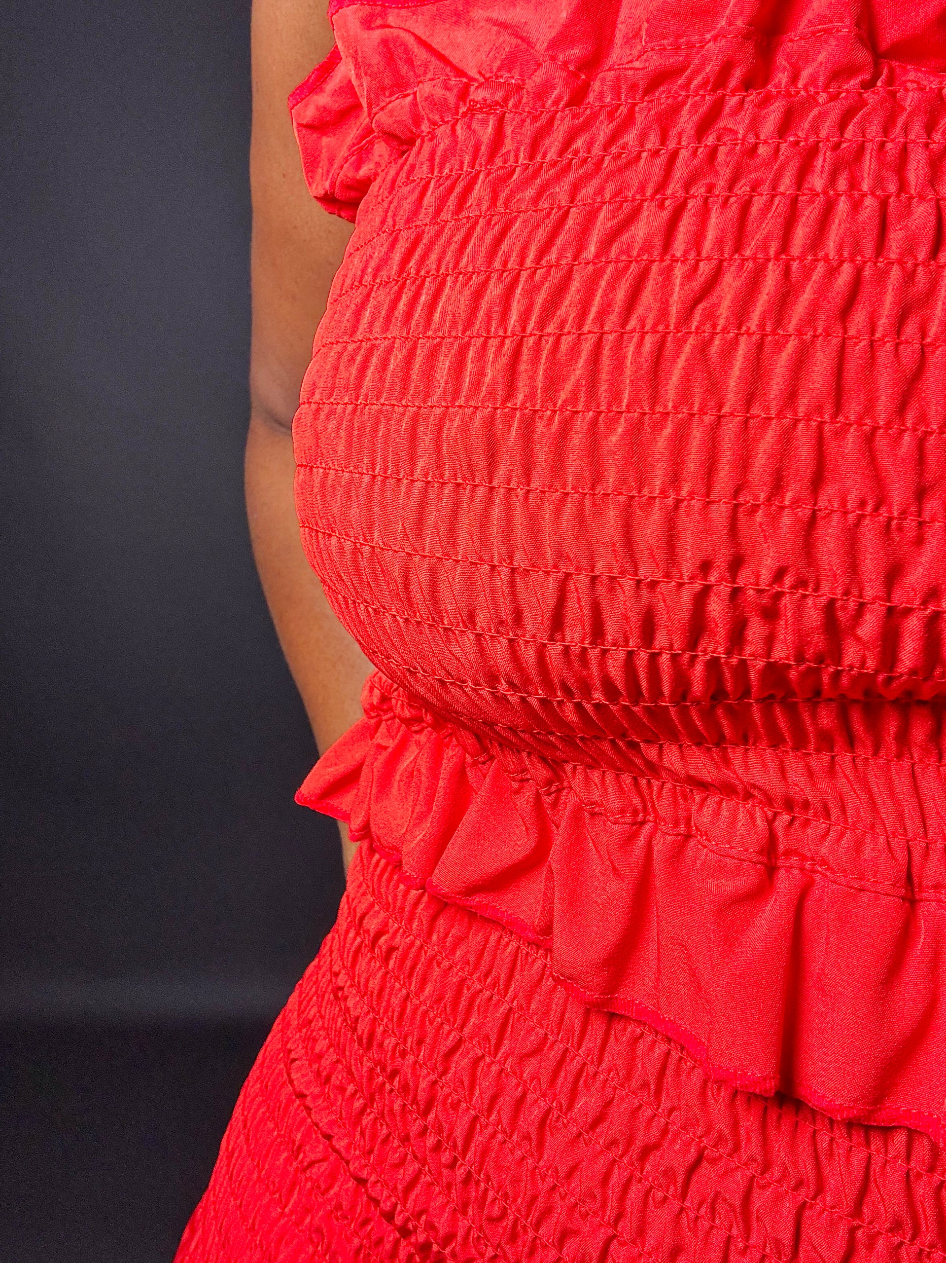  red smocked strapless shirred midi tube dress with smocked bodice and ruffled details on a dark background