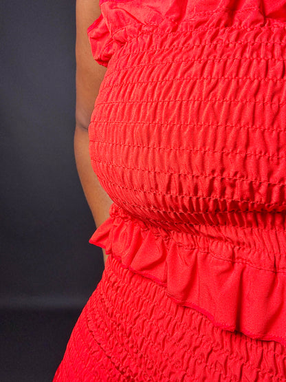  red smocked strapless shirred midi tube dress with smocked bodice and ruffled details on a dark background