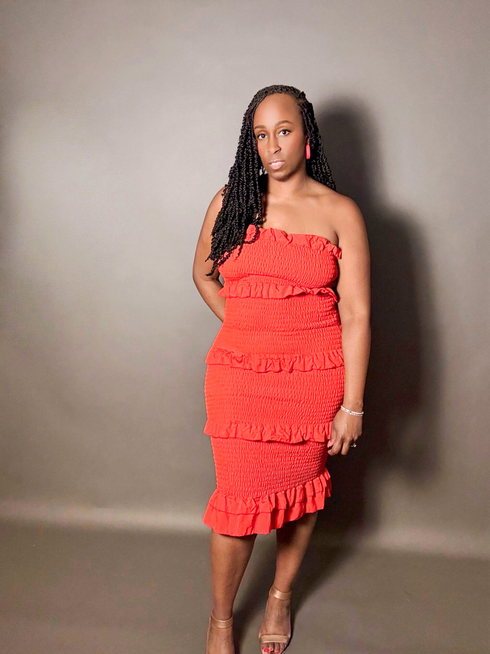 Woman wearing a red smocked strapless shirred midi tube dress with ruffled details against a plain gray background