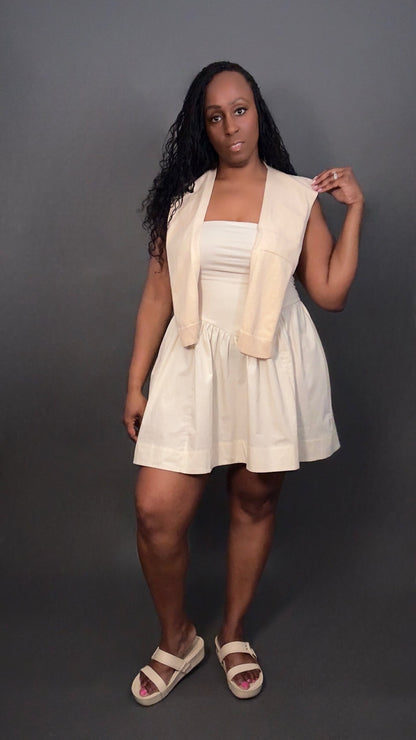 Woman wearing a cream dress with a cream knitted shawl against a dark gray background